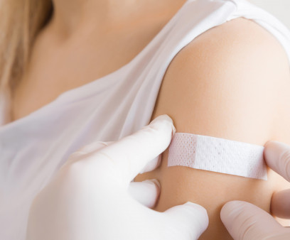 Doctor in white rubber protective gloves putting an adhesive bandage on young woman's arm after scratch on skin or injection of vaccine