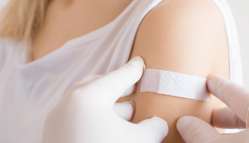 Doctor in white rubber protective gloves putting an adhesive bandage on young woman's arm after scratch on skin or injection of vaccine