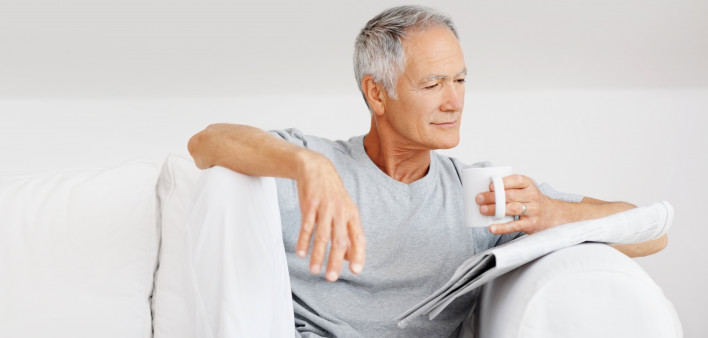 older grey haired man on couch with a coffe much reading the paper