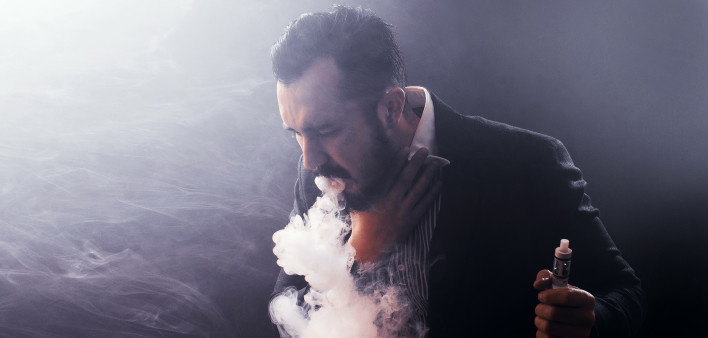 Man coughing out vaponizer holding a vape mod in his hand.