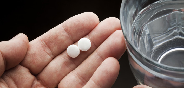 Hands holding two aspirin and a glass of water