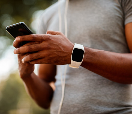 African-American male with smart watch and headphones texting messages on mobile phone during jogging session.