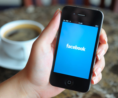 Woman hand holding an Apple iPhone 4 in a coffee shop. iPhone 4 displaying start up screen of Facebook application.