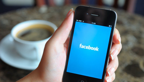 Woman hand holding an Apple iPhone 4 in a coffee shop. iPhone 4 displaying start up screen of Facebook application.