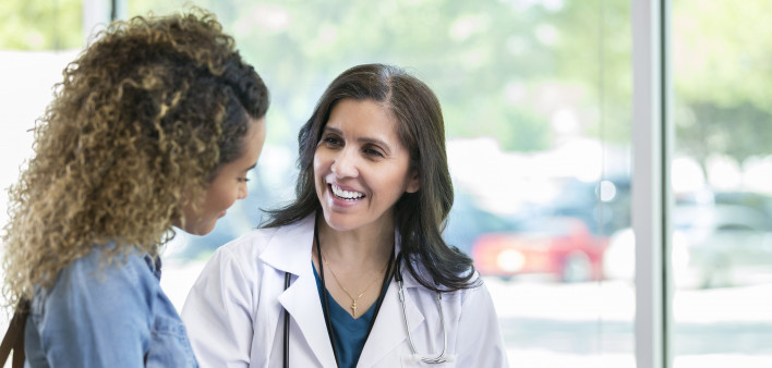 Caring mature female doctor shows test results to a young adult female patient. The doctor is smiling while talking with the patient