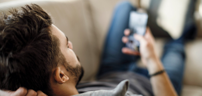 man on couch texing on smart phone