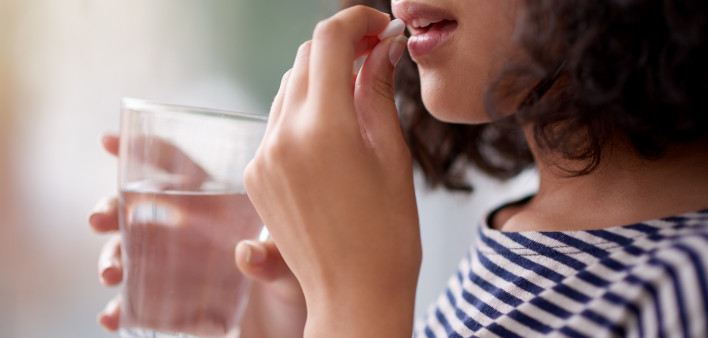 woman taking a pill and holding a glass of water