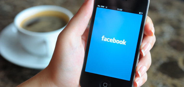 Woman hand holding an Apple iPhone 4 in a coffee shop. iPhone 4 displaying start up screen of Facebook application.