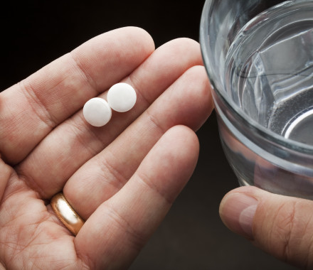 Hands holding two aspirin and a glass of water