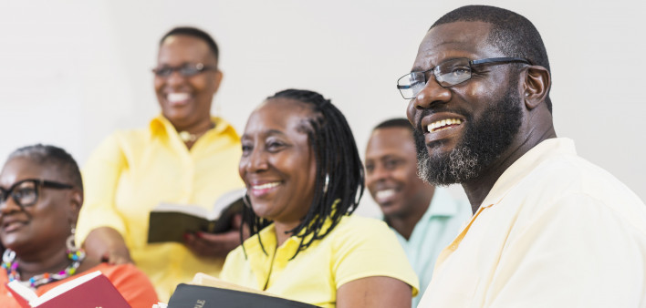 A group of mature African-American men and women holding bibles. They are in a church meeting or bible study group, watching a presentation.