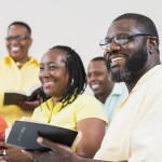 A group of mature African-American men and women holding bibles. They are in a church meeting or bible study group, watching a presentation.
