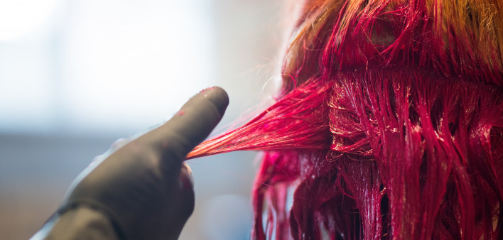 Young woman getting her hair dyed a vivid red in salon