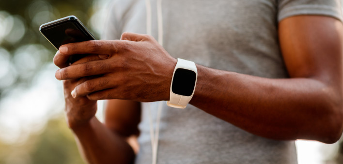 African-American male with smart watch and headphones texting messages on mobile phone during jogging session.