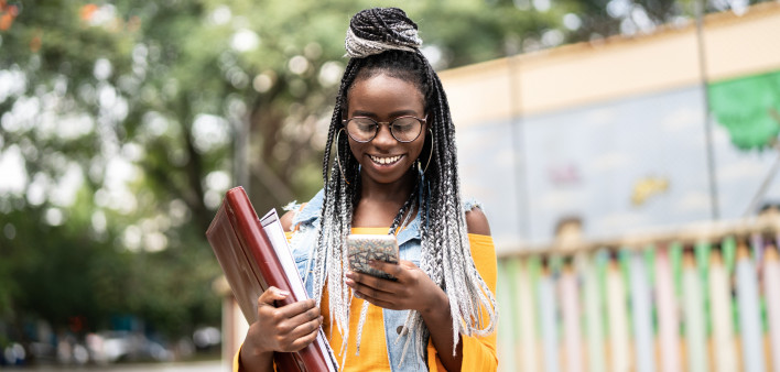 black girl carrying books and using a cell phone