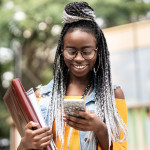 black girl carrying books and using a cell phone