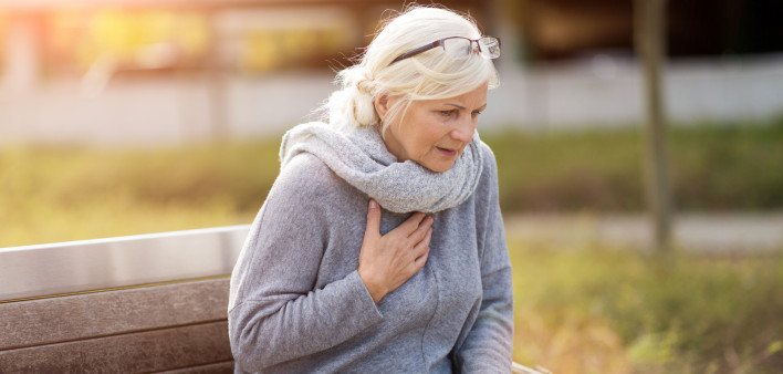 Senior Woman Suffering From Chest Pain While Sitting On Bench