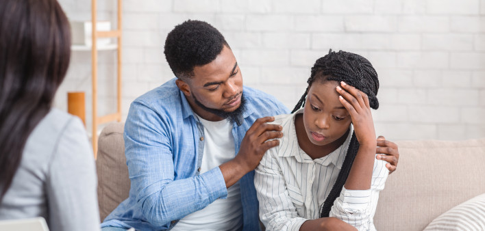 Loving husband supporting his depressed wife during psychotherapy session with counselor