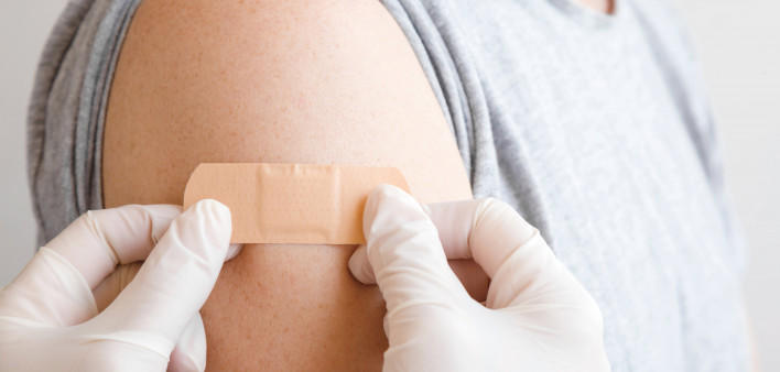 gloved hands applying a band aid to arm