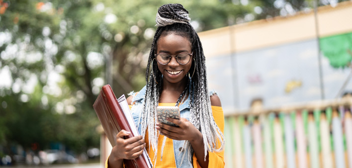 black girl carrying books and using a cell phone