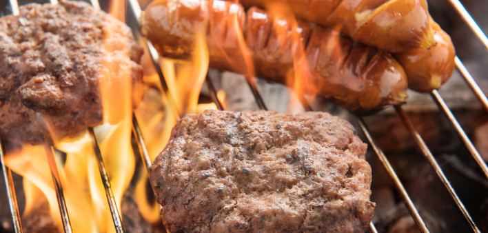 hotdogs and hamburgers on a grill with flames