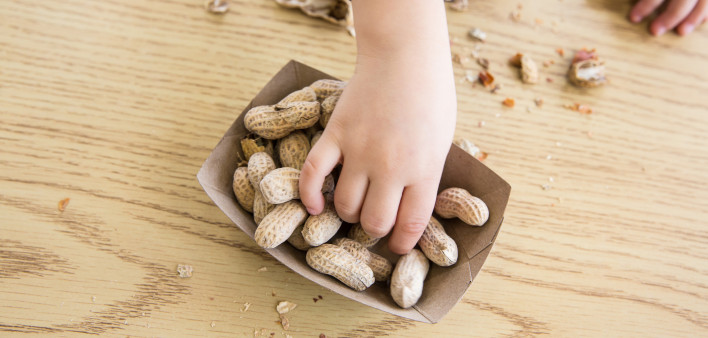 Unrecognizable little boy sits at a table eating peanuts