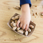 Unrecognizable little boy sits at a table eating peanuts