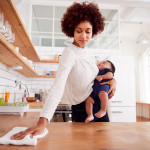 Multi-Tasking Mother Holds Sleeping Baby Son And Cleans In Kitchen