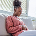 young black girl in pain, sitting on couch holding stomach