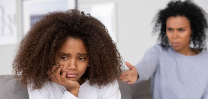 Close up focus african american adolescent girl feels badly melancholic sad and frustrated. On background angry mother accusing scolding reprimanding teen daughter. Teenager behavior problems concept