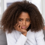 Close up focus african american adolescent girl feels badly melancholic sad and frustrated. On background angry mother accusing scolding reprimanding teen daughter. Teenager behavior problems concept