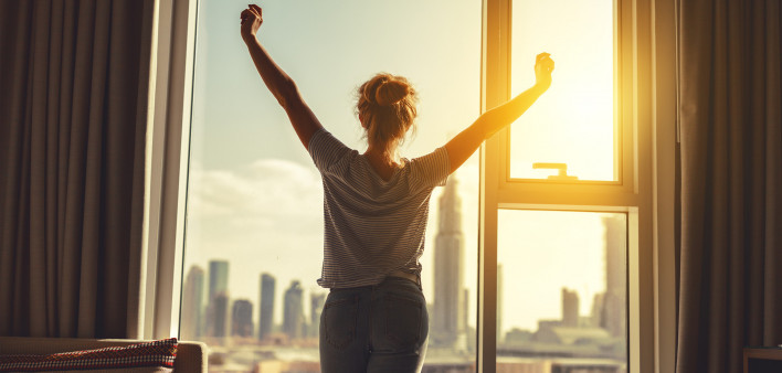 happy woman stretches and opens the curtains at window in morning