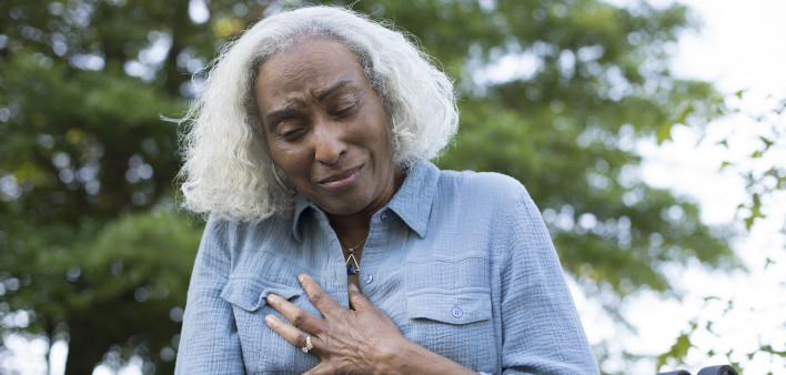 A senior woman makes a pained expression and grabs her chest.