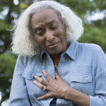 A senior woman makes a pained expression and grabs her chest.