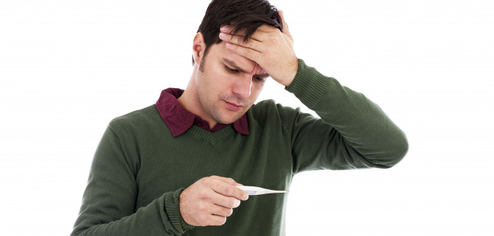 Young man holding his hand to his forehead and holding a thermometer
