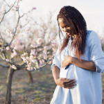 Portrait of a beautiful, young African woman enjoying her pregnancy at the orchard in bloom.
