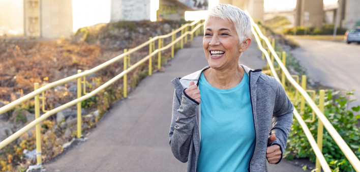 Portrait of elderly woman running in the park in early morning. Photo of Attractive looking gray hair mature woman keeping fit and healthy. Fit mature woman jogging on the pier on a sunny day while.