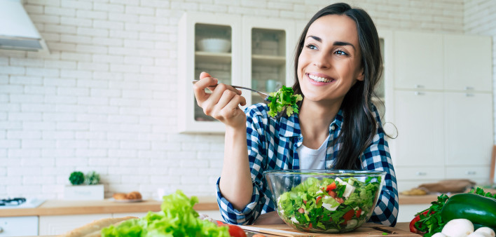 happy cute beautiful young woman while she try tasty vegan salad in the kitchen at home.