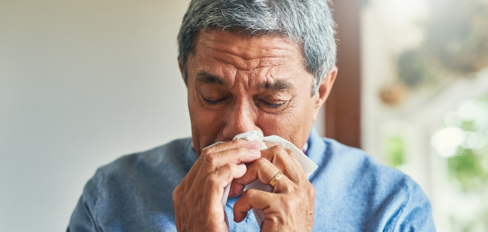 sickly senior man blowing his nose with a tissue at home
