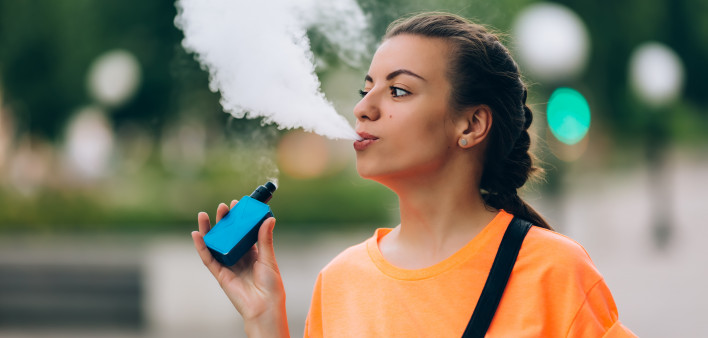 Pretty young hipster woman vape ecig, vaping device at the sunset.