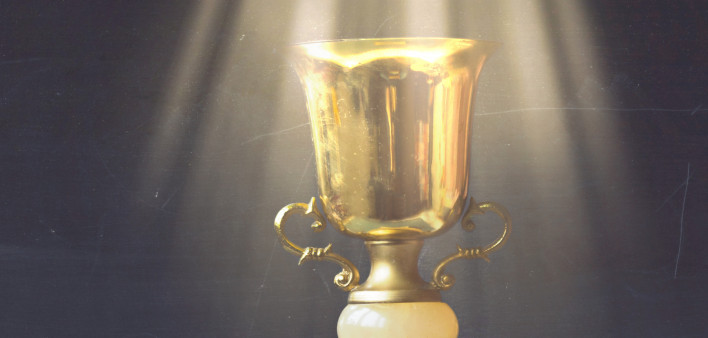 Golden trophy on pile of books, against blackboard, with sun rays over trophy; learning/achievement
