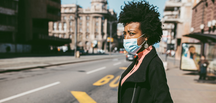 Young Afro American woman standing on city street with protective mask on her face. Virus pandemic and pollution concept.