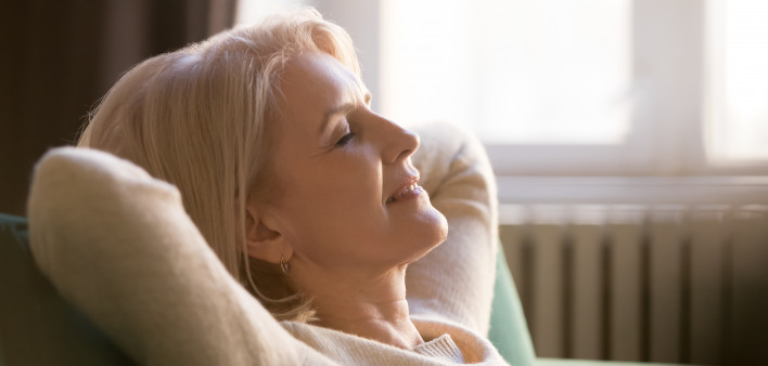 Happy lazy senior old woman relaxing meditating leaning on comfortable sofa at home