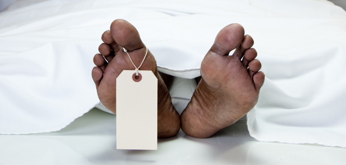 Dead African descent man in morgue with toe tag. Mortician or medical examiner/coroner is covering up the corpse.