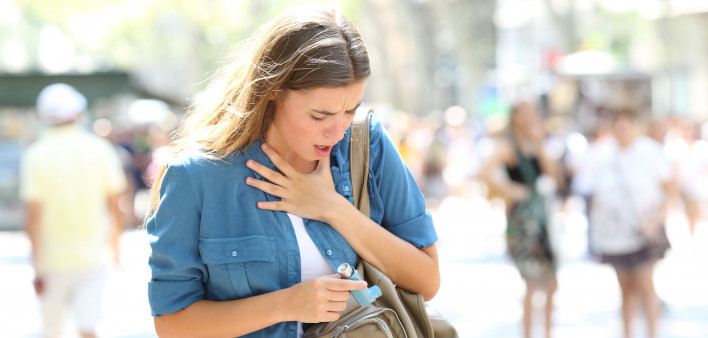 Asthmatic girl suffering an attack and searching the inhaler in a bag in the street