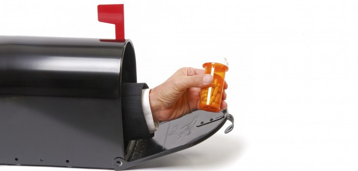 a hand holding a prescription coming out of a mailbox