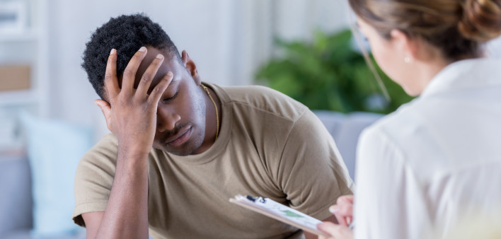 Distraught African American soldier has is head in his hands while talking with a healthcare professional.