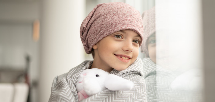 A happy elementary age girl with cancer is wearing a pink scarf on her head.