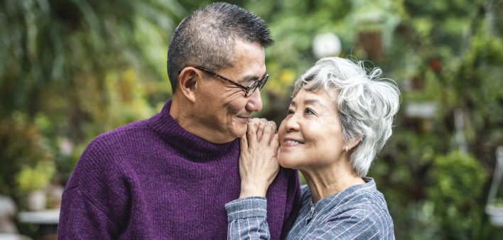 Close-up of smiling senior Chinese woman standing face to face with her contented bespectacled husband.