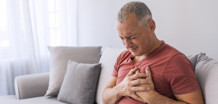 Severe heartache, man suffering from chest pain, having heart attack or painful cramps, pressing on chest with painful expression. Photo of Mature man suffering from chest pain at home during the day.