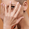 Beautiful young woman with shaved head covering her face with both hands